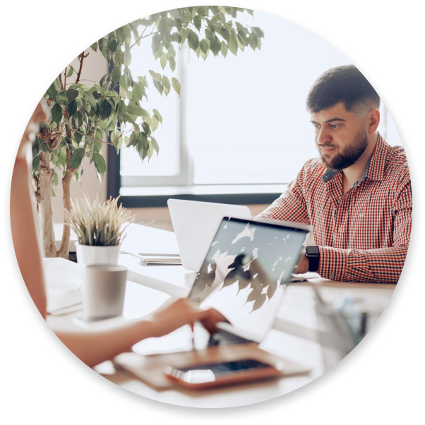 One person using a notebook, and another in the background analyzing papers.